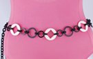 chain belt: white cartwheel disks, smooth and textured black rings, all joined by double black circle links; extension chain comprises stippled black flat right chain links tipped by white plastic ring